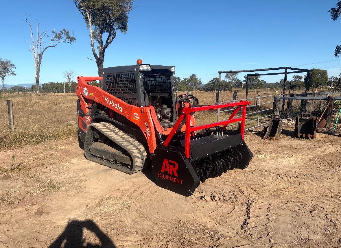 Red Kubota tracked loader with brush cutter attachment on rural ranch property with scattered trees